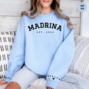 a woman sitting on a bed wearing a blue sweatshirt