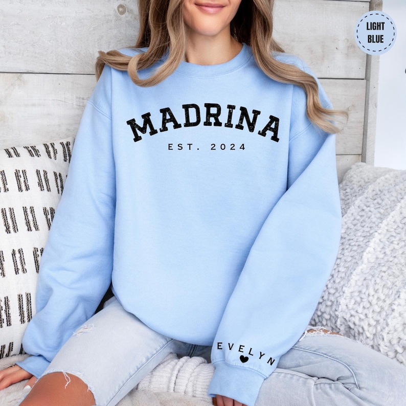 a woman sitting on a bed wearing a blue sweatshirt