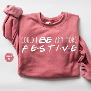 A red sweater with the text "COULD I BE ANY MORE FESTIVE" printed on it.