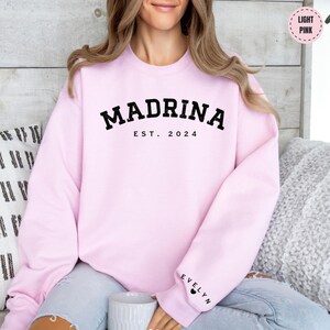 a woman sitting on a couch wearing a pink sweatshirt