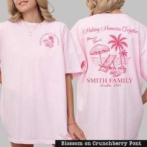 A woman wearing a pink t-shirt with a graphic design on the back, depicting a beach scene with a palm tree, beach chair, and umbrella.