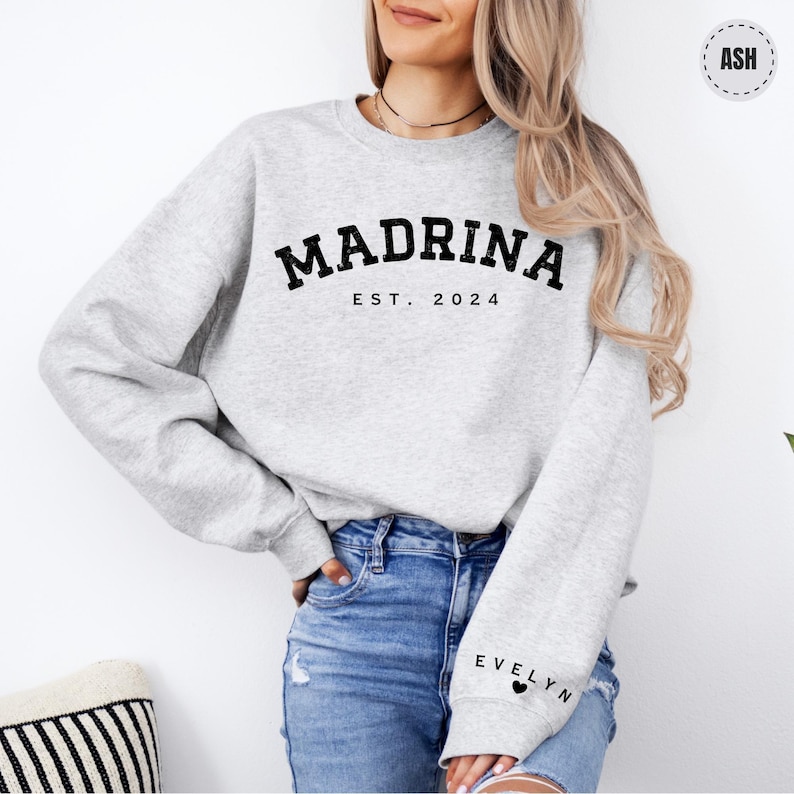 a woman wearing a grey sweatshirt with the word madam on it