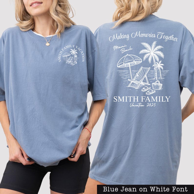 A woman wearing a blue t-shirt with a graphic design on the back, depicting a beach scene with a palm tree, beach chair, and umbrella.