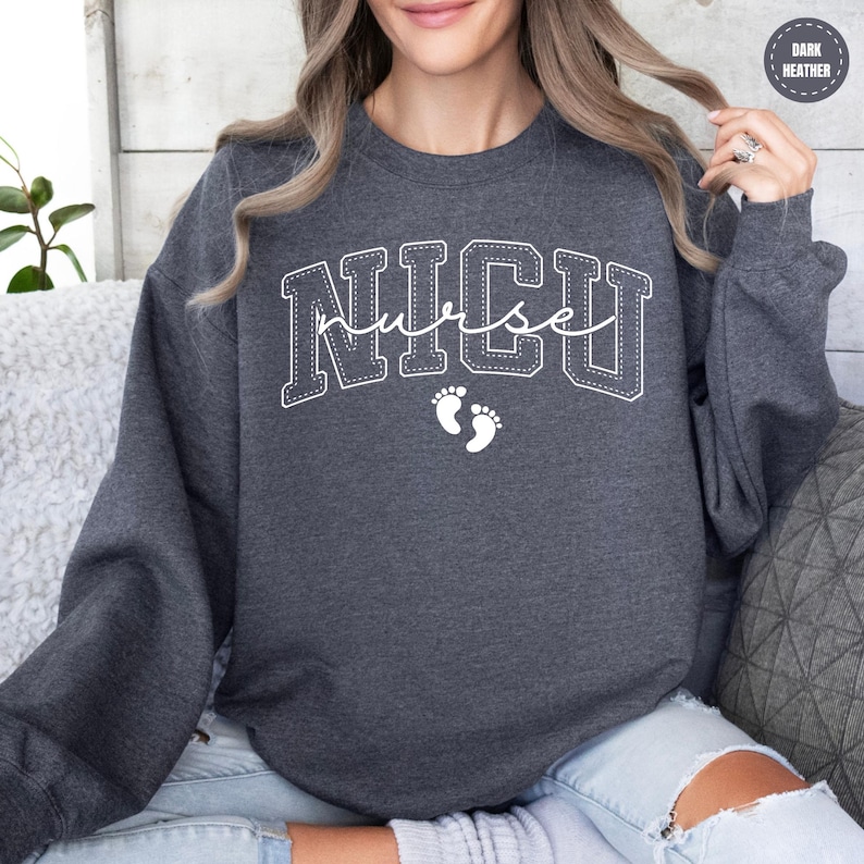 A woman wearing a grey sweatshirt with the word "NICU" printed on it, sitting on a couch.