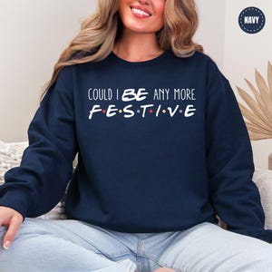 A woman wearing a navy blue sweatshirt with the text "COULD I BE ANY MORE FESTIVAL" printed on it.
