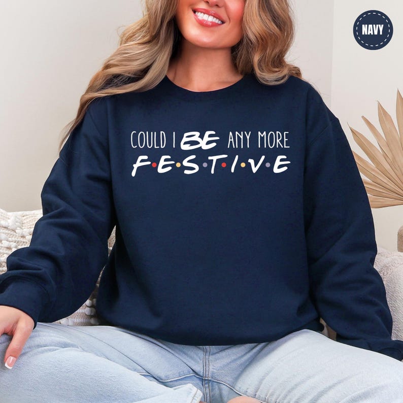 A woman wearing a navy blue sweatshirt with the text "COULD I BE ANY MORE FESTIVAL" printed on it.