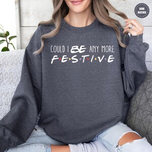 A woman wearing a gray sweatshirt with the text "COULD I BE ANY MORE FESTIVAL" printed on it.