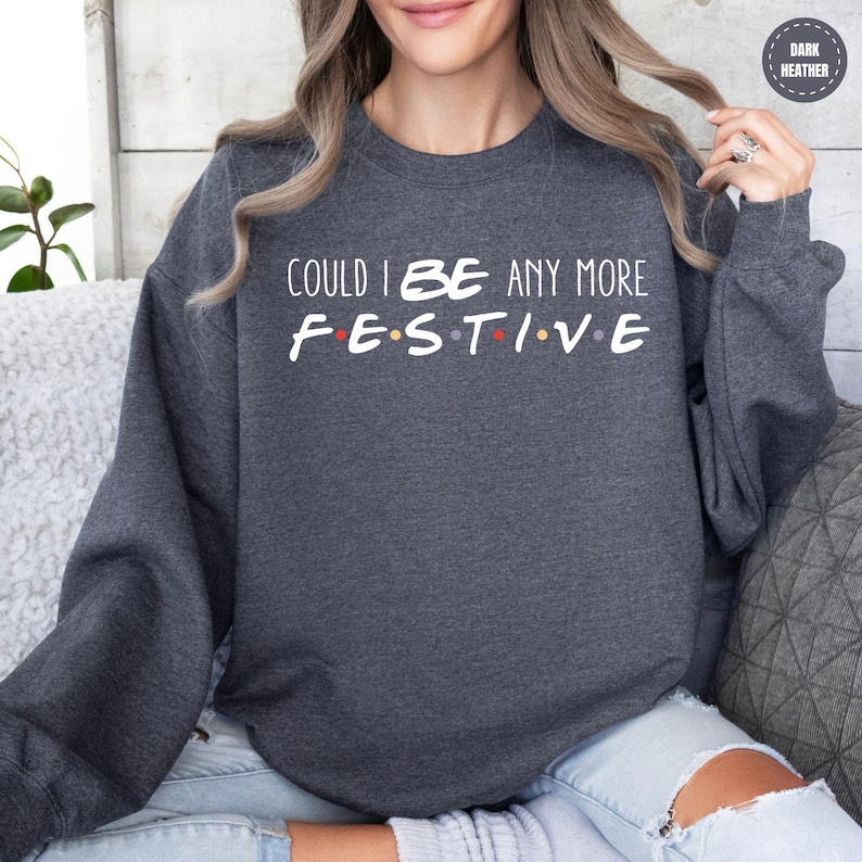 A woman wearing a gray sweatshirt with the text "COULD I BE ANY MORE FESTIVAL" printed on it.