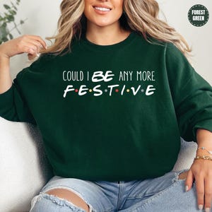 A woman wearing a green sweatshirt with the text "COULD I BE ANY MORE FESTIVE" printed on it.