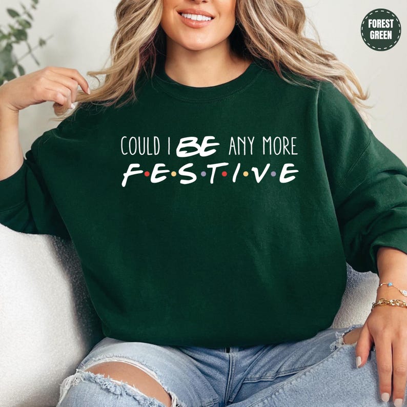A woman wearing a green sweatshirt with the text "COULD I BE ANY MORE FESTIVE" printed on it.