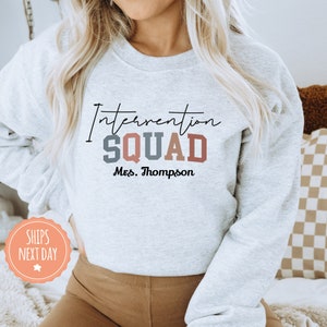 May include: Gray sweatshirt with the text "Intervention Squad" in colorful letters and "Mrs. Thompson" below.