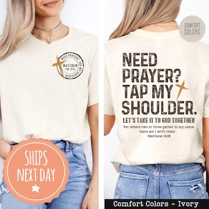 May include: Ivory-colored t-shirt with the text "Need Prayer? Tap My Shoulder." and a cross graphic. The shirt also features the text "Let's take it to God together" and the Bible verse Matthew 18:20.