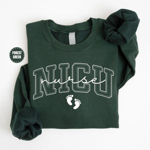 A dark green sweatshirt with the word "NICU" printed on it, along with a pair of white footprints.