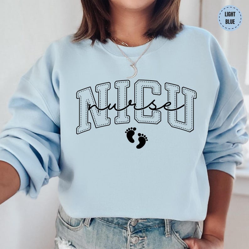 A woman wearing a light blue sweatshirt with the word "NICU" printed on it, along with a pair of jeans.