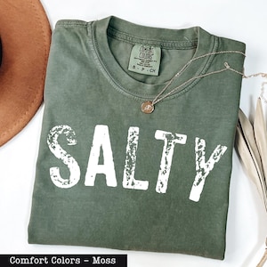 A green t-shirt with the word "SALTY" printed on it, along with a necklace and a brown hat.