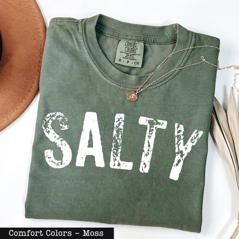 A green t-shirt with the word "SALTY" printed on it, along with a necklace and a brown hat.