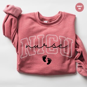 A pink sweatshirt with the word "NICU" printed on it, along with a pair of black footprints below the text.