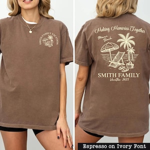 A woman wearing a brown t-shirt with a graphic design on the back, depicting a beach scene with a palm tree, beach chair, and umbrella.