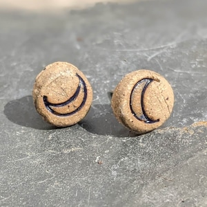 Può includere: Un paio di orecchini in ceramica marrone con un design a mezzaluna. Le lune sono contornate di nero.