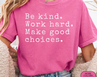 May include: A pink Comfort Colors t-shirt with the text "Be kind. Work hard. Make good choices." in white. The shirt is a solid color and has a crew neck. The shirt is labeled "CRUNCHBERRY" and "MORE COLORS AVAILABLE."