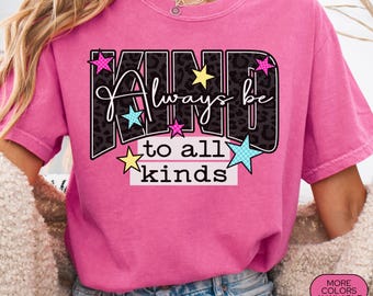 May include: A pink Comfort Colors t-shirt with the words "KIND Always be to all kinds" in a black leopard print design with colorful star accents. The shirt is a crew neck and has short sleeves.