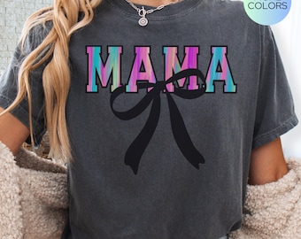May include: A gray t-shirt with a rainbow ombre effect and the word "MAMA" in white letters with a black bow underneath.