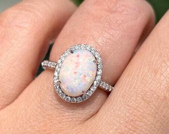 May include: A silver ring with a white opal gemstone surrounded by a halo of smaller clear gemstones.