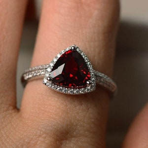 May include: A silver ring with a large, triangular, red gemstone surrounded by smaller, white gemstones.