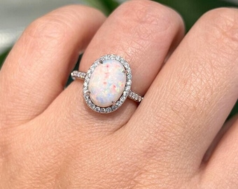 May include: A silver ring with a white opal gemstone surrounded by a halo of smaller clear gemstones.