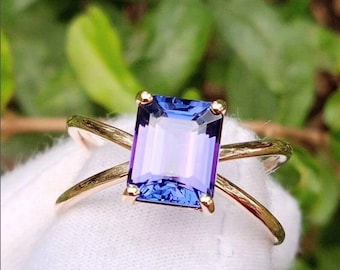 May include: A gold ring featuring a purple and blue emerald-cut gemstone. The ring has a criss-cross design.