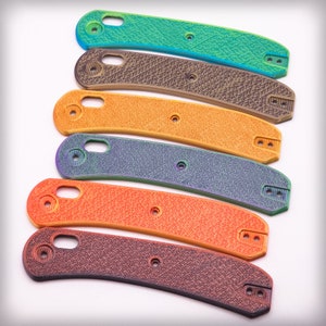 Op de afbeelding: Een set van zes verschillende gekleurde mesbeschermers. De beschermers zijn gemaakt van een getextureerd materiaal en hebben een gebogen vorm. De kleuren zijn teal, bruin, oranje, paars, oranje en bruin.
