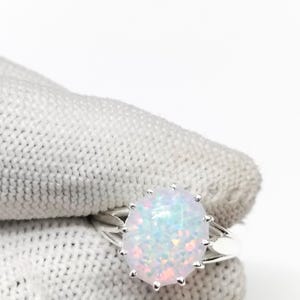 Könnte beinhalten: Ein silberner Ring mit einem ovalen, schillernden Opal-Edelstein. Der Opal zeigt eine Mischung aus Weiß, Rosa und Blau. Das Ringband hat ein geteiltes Design, und der Edelstein ist mit kleinen Zinken befestigt.