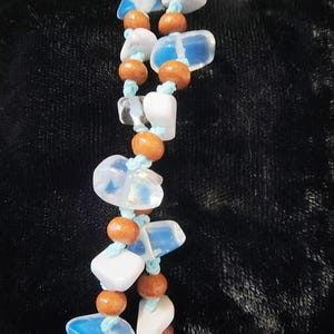Puede incluir: Una pulsera hecha a mano con cuentas de piedras preciosas blancas, azules y transparentes, intercaladas con pequeñas cuentas de madera. Las cuentas están ensartadas en un cordón azul claro, creando un accesorio único y colorido.