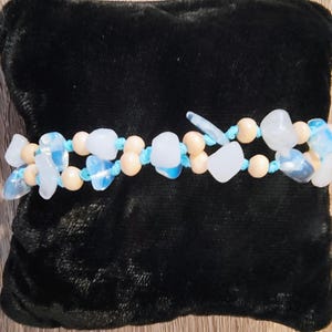 Pode incluir: Um bracelete de duas voltas com contas azuis claras e bege. As contas são enfiadas em um cordão azul.