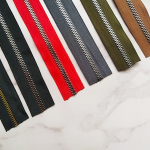 May include: Assortment of six zipper tapes in various colors, including black, red, gray, green, and brown. Each tape features a silver metal zipper.