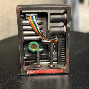 May include: A small, black, rectangular box with a warning label that reads "High Voltage Present". The box has a clear window that reveals a circuit board with wires and components.