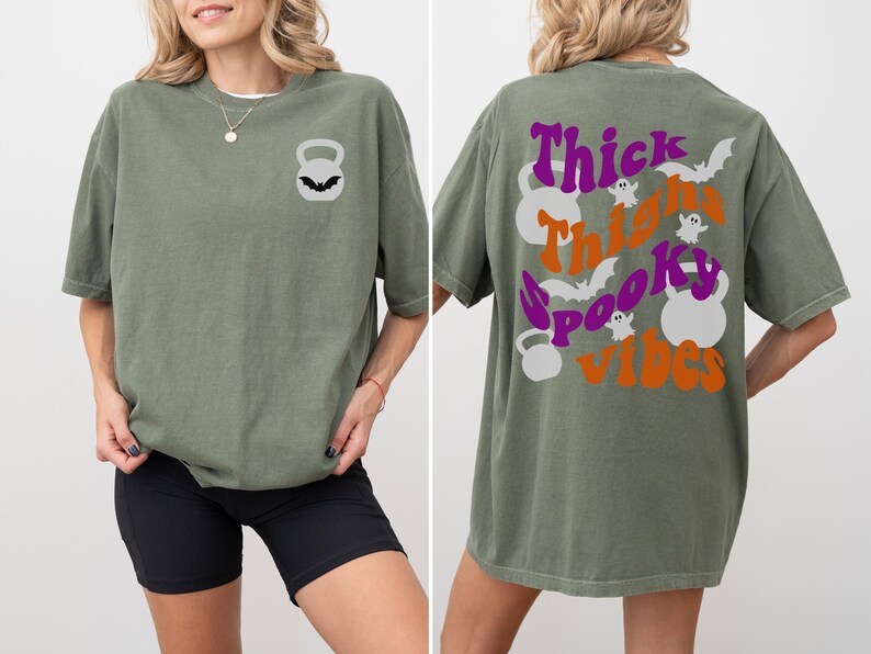 May include: A green oversized t-shirt with a black kettlebell graphic on the front and the text "Thick Thighs Spooky Vibes" with a purple and orange color scheme on the back.