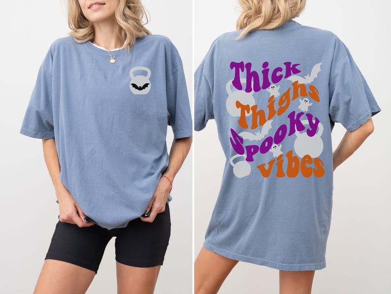 May include: A light blue oversized t-shirt with a graphic print on the back that says "Thick Thighs Spooky Vibes" with bats and ghosts. The front of the shirt has a small graphic of a kettlebell with a bat on it.