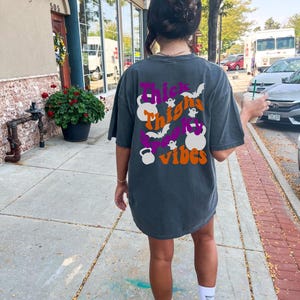 May include: A dark gray t-shirt with a graphic print that says "Thick Thighs Spooky Vibes" with a ghost and bats. The graphic also includes a purple and orange kettlebell.