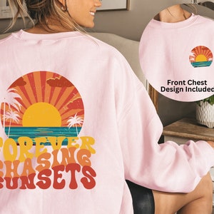 Puede incluir: Sudadera rosa con un gr&aacute;fico de puesta de sol retro y el texto "FOREVER CHASING SUNSETS" impreso en la espalda. El dise&ntilde;o del pecho delantero tambi&eacute;n est&aacute; incluido.