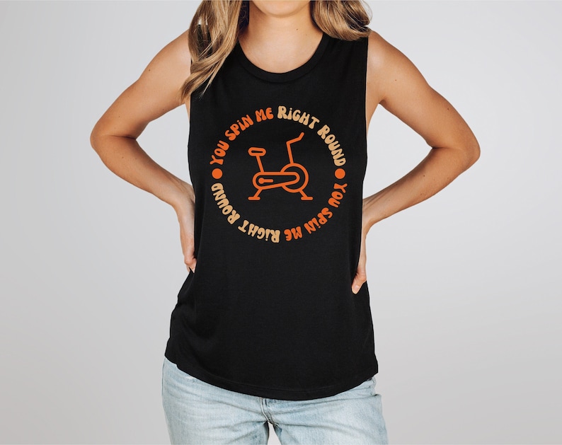 May include: Black sleeveless tank top with orange text and a stationary bike graphic. The text reads "YOU SPIN ME RIGHT ROUND" in a circular design around the bike. A casual fitness-themed top.