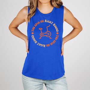 May include: A sleeveless blue tank top with the text "YOU SPIN ME RIGHT ROUND" encircling an orange illustration of a stationary exercise bike. The text and graphic are centered on the front of the top.