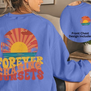 Puede incluir: Una sudadera azul claro con un gr&aacute;fico de puesta de sol retro y el texto "FOREVER CHASING SUNSETS" impreso en la espalda. La parte delantera de la sudadera presenta una versi&oacute;n m&aacute;s peque&ntilde;a del gr&aacute;fico de puesta de sol.