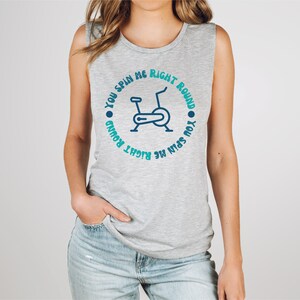 May include: A gray sleeveless shirt with the text "YOU SPIN ME RIGHT ROUND" encircling a blue stationary bike graphic. The shirt is made of a soft material and is suitable for workouts or casual wear.