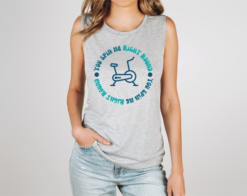 May include: A gray sleeveless shirt with the text "YOU SPIN ME RIGHT ROUND" encircling a blue stationary bike graphic. The shirt is made of a soft material and is suitable for workouts or casual wear.