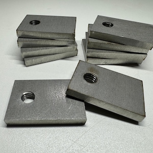 May include: A stack of eight silver metal plates with a hole in the centre of each plate. The plates are rectangular and have a slightly textured surface.