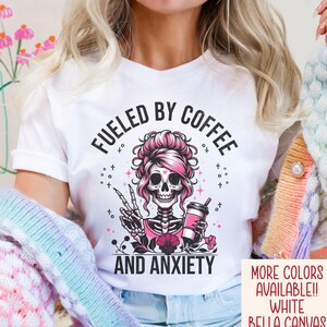 May include: White t-shirt with a pink skeleton holding a coffee cup and the text "Fueled by Coffee and Anxiety".