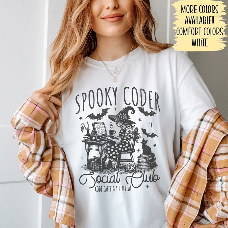 May include: White t-shirt with a black and white illustration of a witch coding on a computer. The text "Spooky Coder Social Club" is printed on the shirt. The text "Code Caffeinate Repeat" is printed below the illustration.