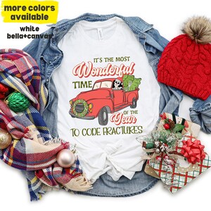 May include: White t-shirt with a red truck and a skeleton driving. The truck has a Christmas tree in the back. The text on the shirt reads "It's the most Wonderful Time of the Year to Code Fractures".