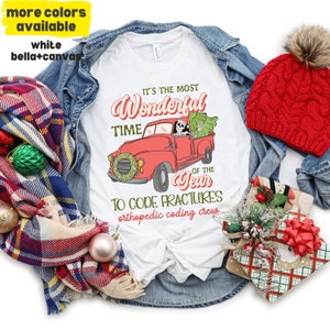 Puede incluir: Camiseta blanca con un camión rojo que lleva un árbol de Navidad y un conductor esqueleto. El texto dice "Es la época más maravillosa del año para codificar fracturas, equipo de codificación ortopédica".
